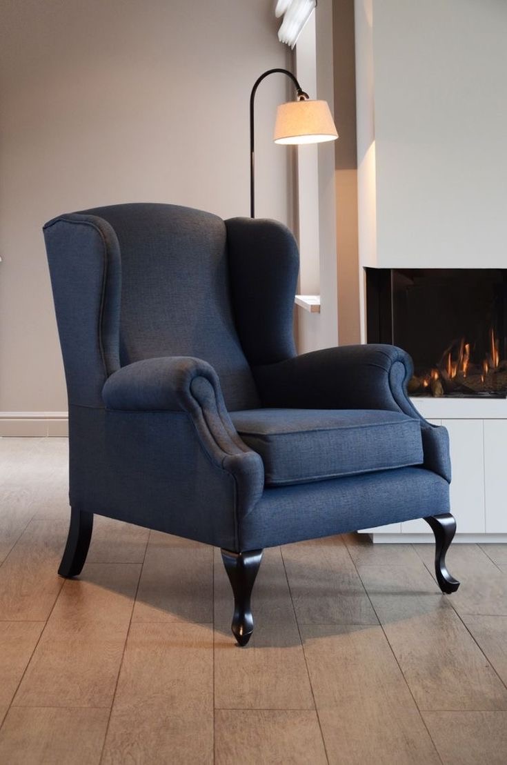 A reupholstered navy wingback armchair beside a fireplace